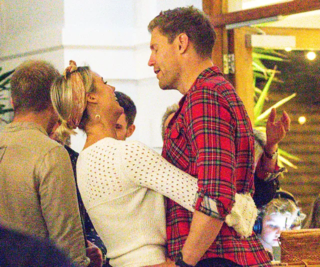 A couple smiling and embracing warmly at a social gathering, both appearing happy and engaged with each other.