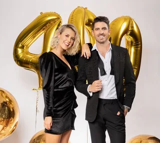 A woman in a black dress and a man in a suit pose with gold balloons forming "400".