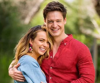 A couple smiling and embracing outdoors, with the woman in a blue top and the man in a red shirt.