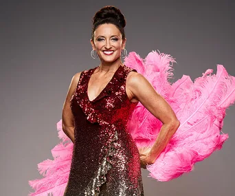 A woman in a red sequin dress with bright pink feathers, smiling and posing confidently.