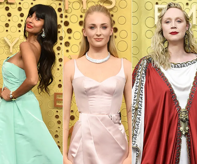 Three women at the 2019 Emmys red carpet in elegant gowns, posing against a gold backdrop.