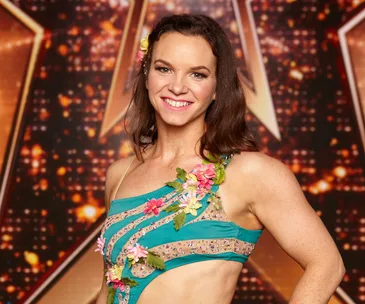 Woman in a floral-adorned turquoise dress smiling against a sparkling background.