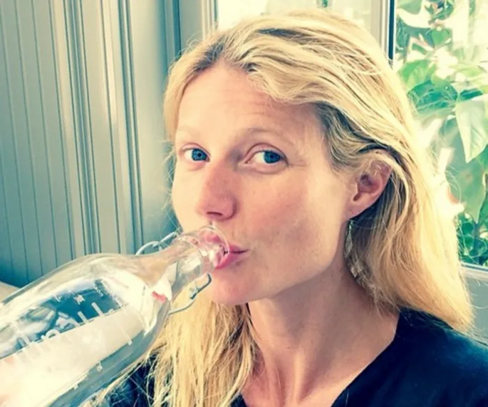 A woman drinking water from a bottle indoors.