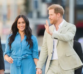 Prince Harry and Meghan Markle walking hand in hand, with Harry waving to the crowd.