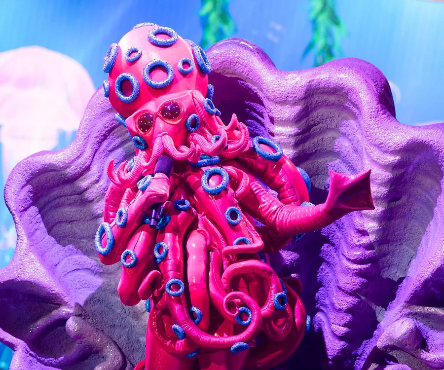 Pink and purple octopus costume with tentacles and blue rings on "The Masked Singer" stage.