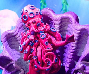 Pink and purple octopus costume with tentacles and blue rings on "The Masked Singer" stage.