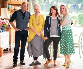 Four people smiling in a cozy kitchen setting with colorful bunting overhead.