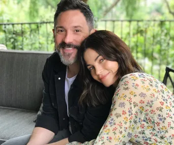 Couple sitting on a sofa outdoors, smiling, with green foliage in the background.