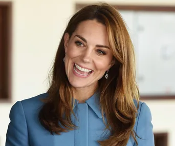 A person smiling and wearing a blue coat with long brown hair and earrings.