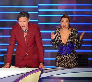 Judges on "The Masked Singer" reacting with surprise, standing at a desk, with a colorful background.