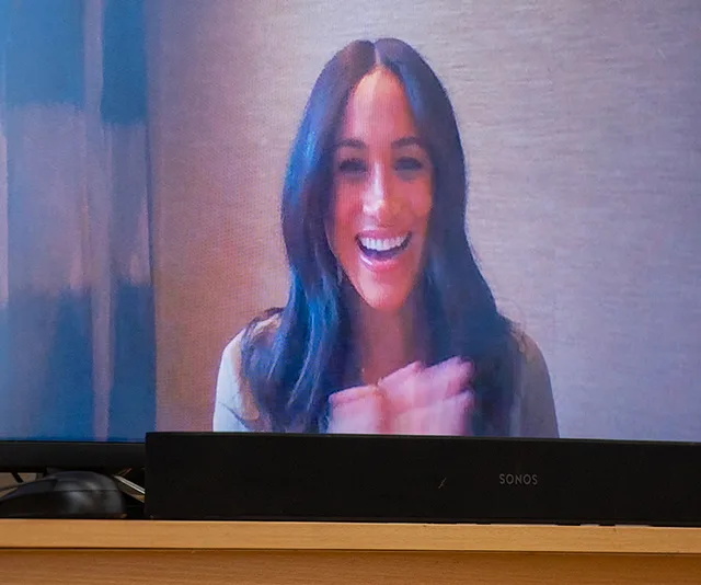 Smiling woman on video call clapping hands, shown on a TV screen.