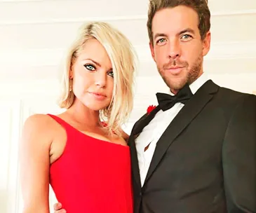 A couple dressed elegantly, with the woman in a red dress and the man in a black tuxedo, standing close together.