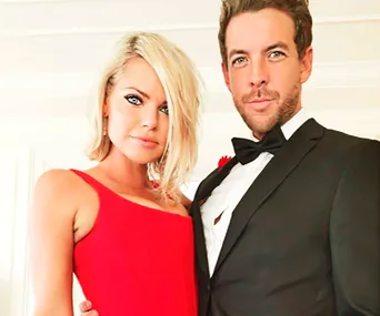 A couple dressed elegantly, with the woman in a red dress and the man in a black tuxedo, standing close together.
