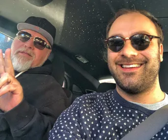 Two men in sunglasses taking a selfie in a car; one making a peace sign.