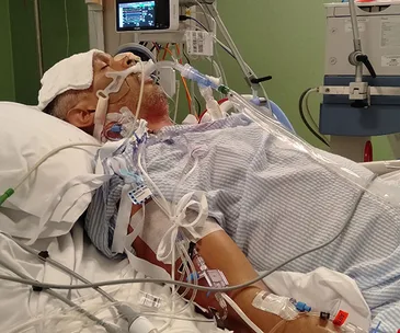 A patient in hospital connected to tubes and monitors, possibly receiving intensive care.