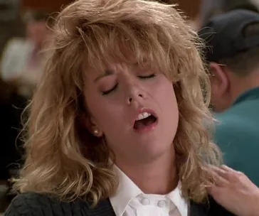 Woman with blonde hair and expressive face, eyes closed, in a crowded setting.