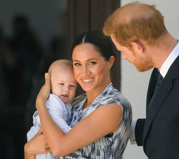 A family with a woman holding a baby, with a man looking on, all smiling and dressed formally.