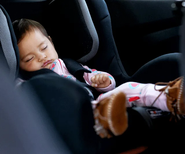 Baby sleeping in a car seat, wearing a colorful onesie and brown boots.