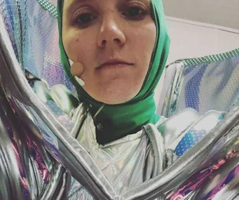 An individual in a colorful metallic costume with a green headpiece, likely from "The Masked Singer."