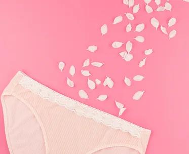 Lacy women's underwear on pink background with scattered white flower petals.