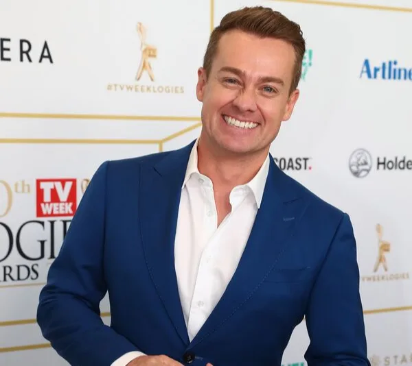 Smiling man in blue suit at the 60th TV Week Logie Awards, standing with hand in pocket.