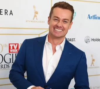 Smiling man in blue suit at the 60th TV Week Logie Awards, standing with hand in pocket.