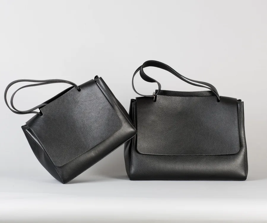 Two stylish black leather handbags with long straps against a plain background.