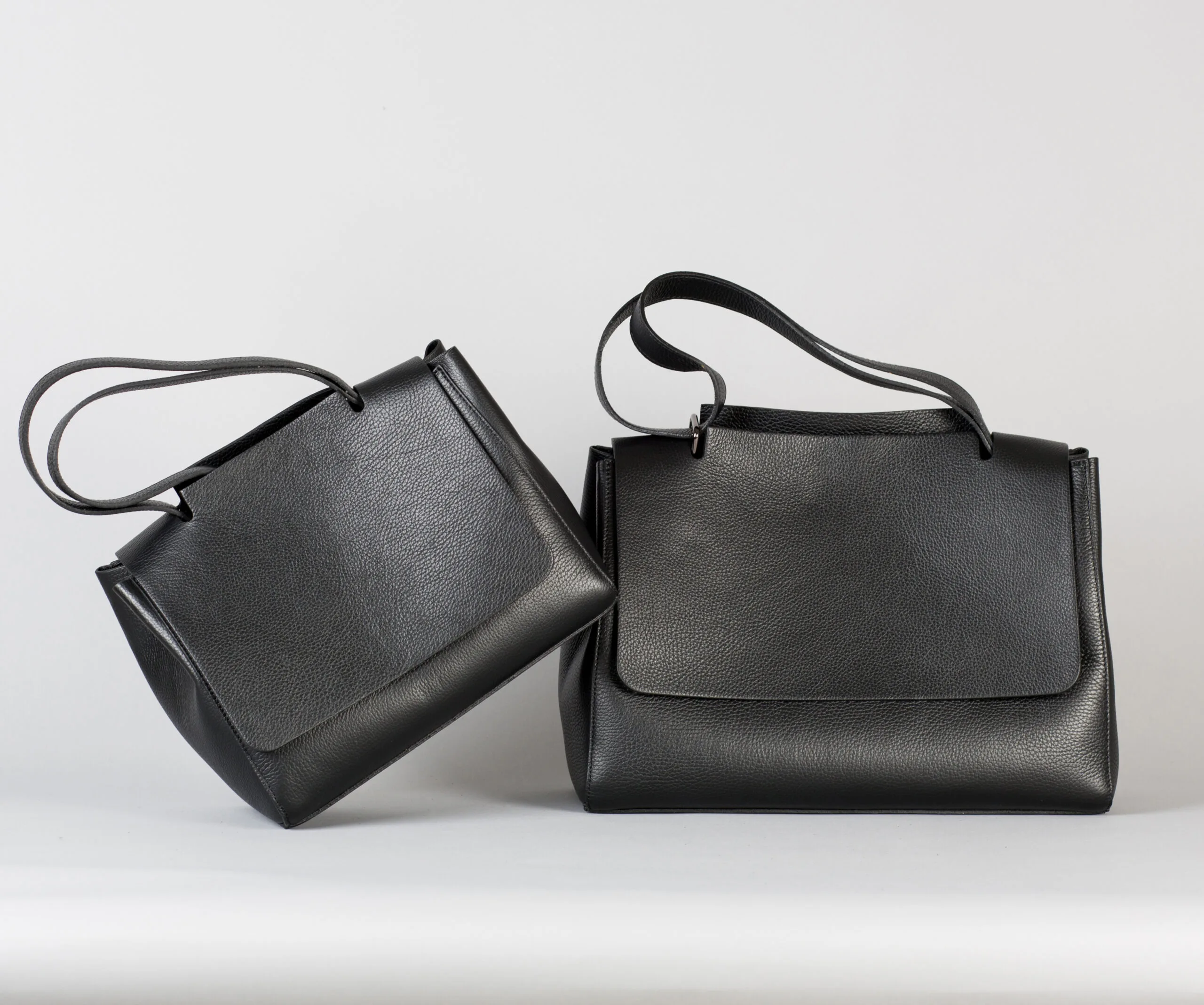 Two stylish black leather handbags with long straps against a plain background.