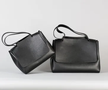 Two stylish black leather handbags with long straps against a plain background.