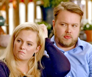 A man and woman sit together, both appearing contemplative and serious in a discussion setting.