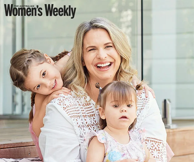 A smiling woman with two young children, one on each side, outdoors.