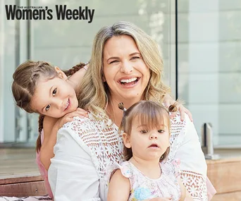 A smiling woman with two young children, one on each side, outdoors.