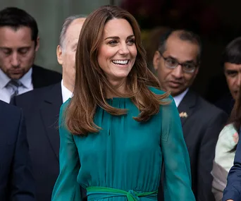 A woman in a green dress, smiling, surrounded by people at an event.