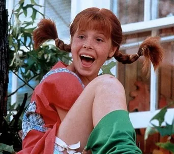 Young girl with red pigtails and a joyful expression, wearing colorful clothes, sitting outdoors.