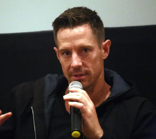 Actor in a hoodie, speaking into a microphone at an event.