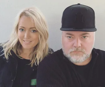 A man in a black cap with a beard and a woman with blonde hair smiling, posed against a plain background.