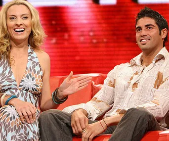 Two people sitting on a red couch, smiling and engaged in conversation. They appear relaxed and casual.