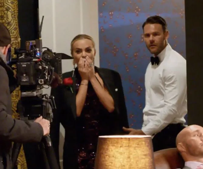 Bachelorette star shocked as she stands next to a man in a white shirt, with a camera crew capturing the moment.