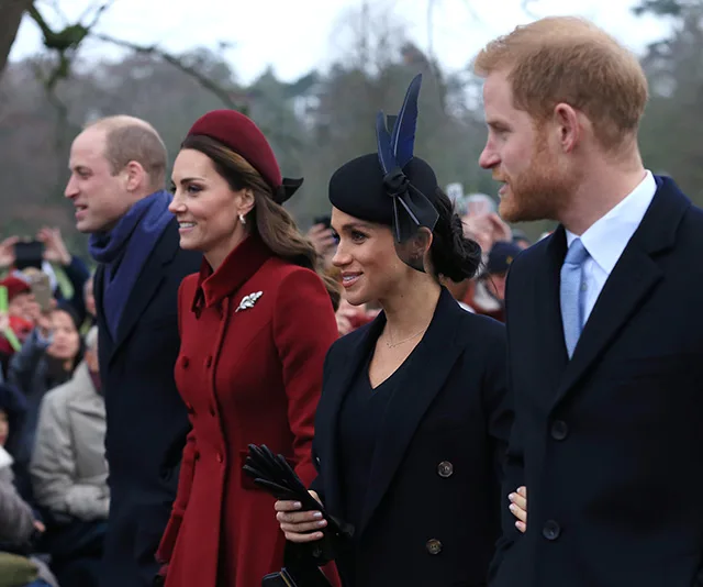 Two couples walking outdoors, dressed formally, surrounded by a crowd and trees in the background.