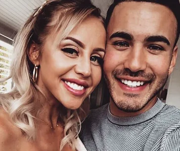 Two people smiling closely in a selfie, indoors, with warm lighting.