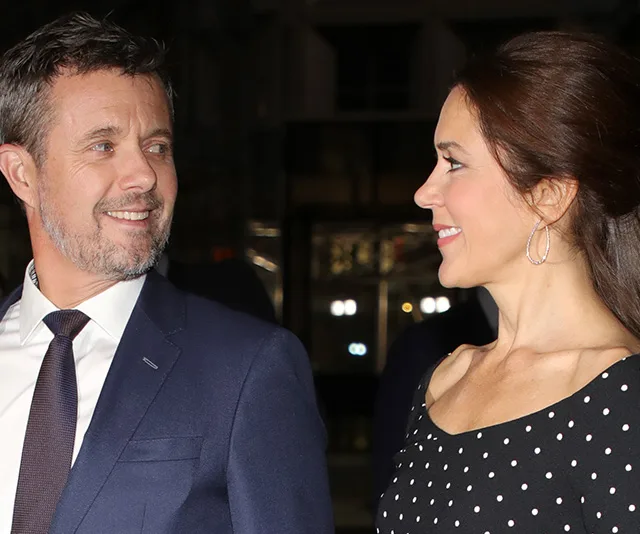 Two people dressed formally, with one wearing a black polka dot dress, smiling at each other.