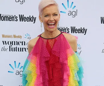 Smiling woman in a vibrant rainbow dress at a "Women's Weekly" event backdrop.