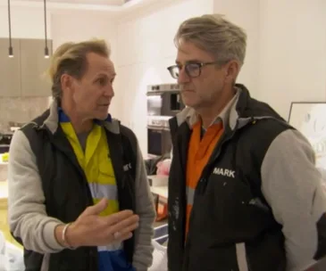 Two men in construction attire having a discussion in a modern kitchen setting.