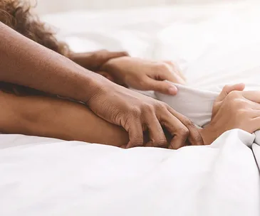A close-up of hands holding gently under white bed covers, conveying intimacy and tenderness.