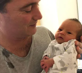 A person holding a baby dressed in an elephant-patterned onesie, smiling affectionately.