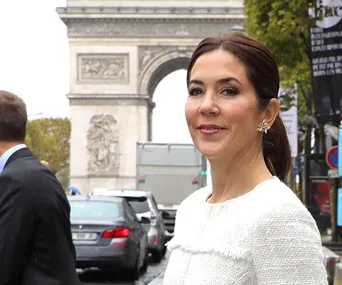 Woman in a white dress smiling near the Arc de Triomphe on a Paris street.