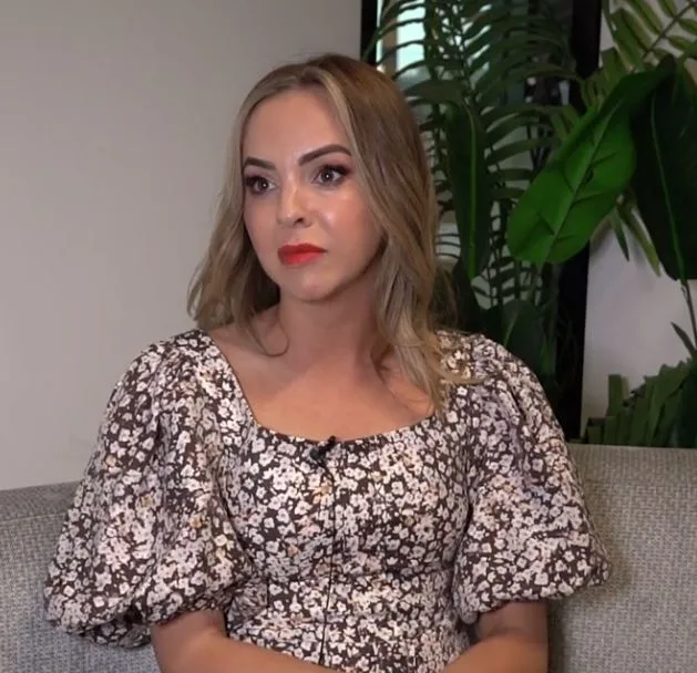 Woman in a floral dress seated on a couch, looking thoughtfully to the side.