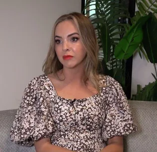Woman in a floral dress seated on a couch, looking thoughtfully to the side.