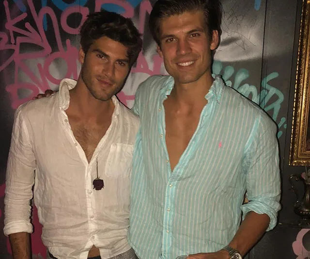 Two men smiling in front of graffiti wall, one in a white shirt, the other in a light striped shirt.