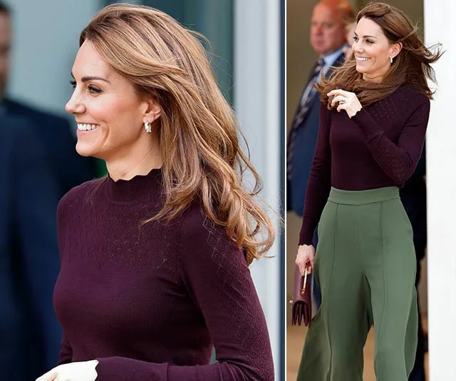 Kate Middleton in a burgundy top and green pants, smiling while walking outdoors.
